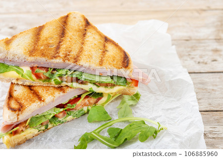 Panini sandwich with ham, cheese, tomato and arugula on wooden table 106885960