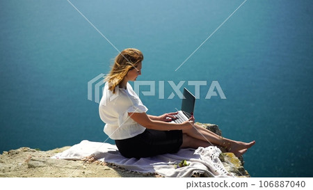 Freelance woman sea. working on a laptop by the sea, typing away on the keyboard while enjoying the beautiful view, highlighting the idea of remote work. 106887040