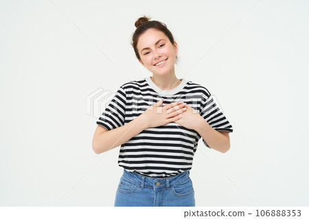 Image of beautiful woman in casual clothes, holds hands on heart and smiles, express gratitude, being thankful, stands over white background Image of beautiful woman in casual clothes, holds hands on heart and smiles, express gratitude, being thankful, stands over white background 106888353
