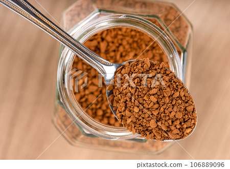 Top view on spoon with instant granulated coffee over a jar on a wooden background. 106889096