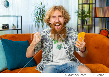 Caucasian young man at home use smartphone celebrating success victory, winning, play online game 106889646