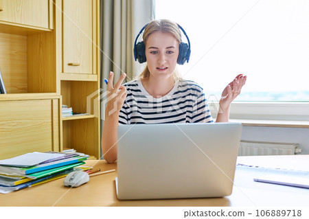 Teenage girl high school student in headphones having video conference on laptop Teenage girl high school student in headphones having video conference on laptop 106889718