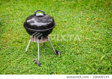 Black grill in the backyard rain green field. Preparing for barbeque party. Black grill in the backyard rain green field. Preparing for barbeque party. 106890145