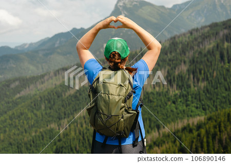 Woman showing heart shape on nature green background. Happy Girl wearing green hat with backpack. Freedom, happiness, travel and vacations concept, outdoor activities Woman showing heart shape on nature green background. Happy Girl wearing green hat with backpack. Freedom, happiness, travel and vacations concept, outdoor activities 106890146