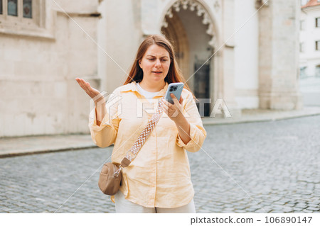 Sad pensive 30s girl with phone standing on city street. Negative people emotion. Upset young woman is using a smartphone outdoors Sad pensive 30s girl with phone standing on city street. Negative people emotion. Upset young woman is using a smartphone outdoors 106890147