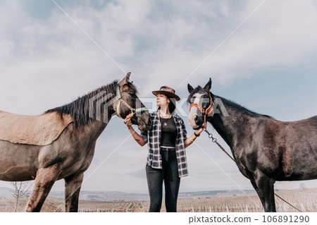 Young happy woman in hat with her horse in evening sunset light. Outdoor photography with fashion model girl. Lifestyle mood. Concept of outdoor riding, sports and recreation. Young happy woman in hat with her horse in evening sunset light. Outdoor photography with fashion model girl. Lifestyle mood. Concept of outdoor riding, sports and recreation. 106891290