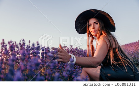 Woman lavender field. Happy carefree woman in black dress and hat with large brim walking in a lavender field during sunset. Perfect for inspirational and warm concepts in travel and wanderlust. 106891311