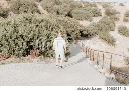 Happy Middle aged couple or friends practicing nordic walking in park near sea. Mature couple with trekking poles walking, practicing Nordic walking outdoors. Aging youthfully and sport concept 106891540