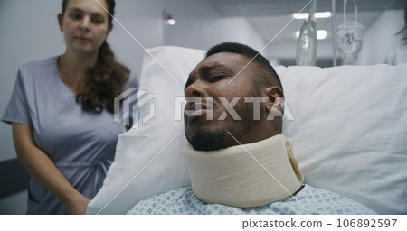 Young nurse transports injured middle aged man to hospital ward 106892597
