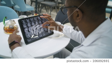 African American doctor examines MRI or CT scan using digital tablet in clinic cafe African American doctor examines MRI or CT scan using digital tablet in clinic cafe 106892691