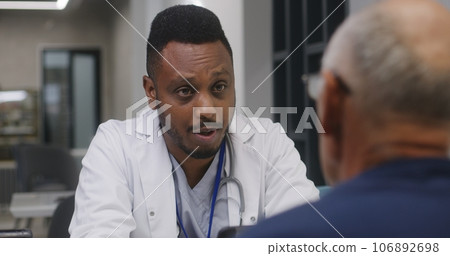African American doctor discusses treatment with elderly patient in clinic cafe 106892698