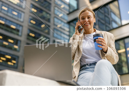 Focused woman manager talking with client and work on laptop on modern office building background 106893306