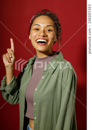Portrait of excited young woman holding index finger up with great new idea on red studio background Portrait of excited young woman holding index finger up with great new idea on red studio background 106893363