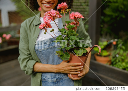 Close up of woman gardener holding flower pot while standing on greenhouse yard background 106893455