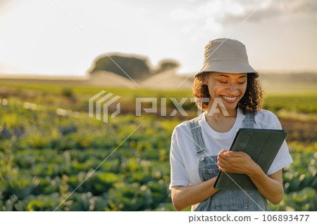 Smiling woman farmer making notes in tablet while works in field. Agricultural business concept 106893477