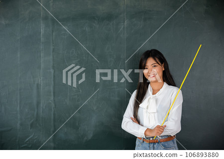 Back to school concept. Asian female teacher smiling with wooden stick on front blackboard at school in classroom, Happy beautiful young woman standing hold pointer looking to camera, Education Back to school concept. Asian female teacher smiling with wooden stick on front blackboard at school in classroom, Happy beautiful young woman standing hold pointer looking to camera, Education 106893880