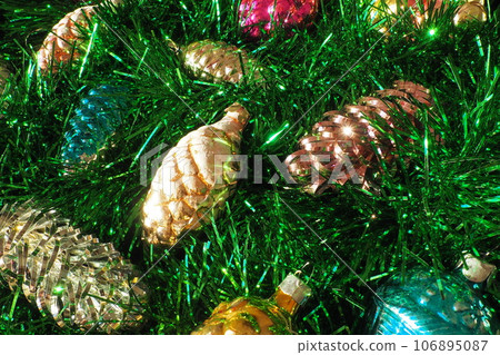 Multi-colored glass cones on green Christmas tree tinsel. Beautiful Christmas toys and decorations as a background. Red, yellow, green and pink shiny new year and christmas figurines. 106895087