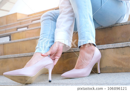woman wearing high heels She had ankle pain and cramps in her legs and ankles from high heels. She sat on the stairs and she held her leg. And she relieved the pain by squeezing her ankles. 106896121