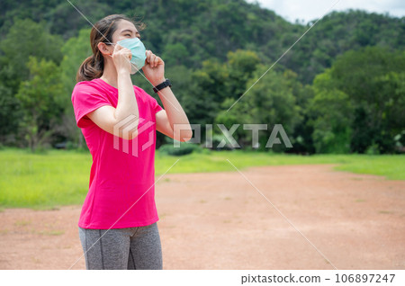 Woman wearing mask while going outdoor in covid-19 pandemic outbreak. Wear a face mask when you're running in an area where social distancing is hard to maintain. 106897247