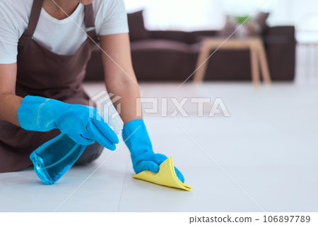 Maid wearing gloves and using cleaner spray and microfiber cloth to wipe a dust on the floor 106897789