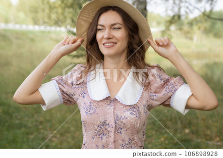A young beautiful woman in a dress and holding a hat with her hands and reading a book in nature. Romantic and vintage photo of a beautiful girl. Reading and relaxation 106898928