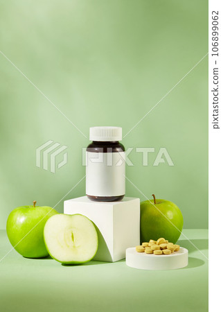 Medicine bottle standing on white podium with green apple surrounded. Some pills are arranged. Medicine, treatments and healthcare with Green Apple (Malus domestica) extract Medicine bottle standing on white podium with green apple surrounded. Some pills are arranged. Medicine, treatments and healthcare with Green Apple (Malus domestica) extract 106899062