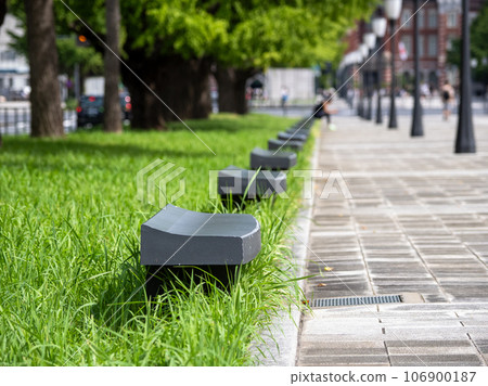 A bench on the sidewalk surrounded by street trees and green grass (Gyukiyuki Dori, Chiyoda-ku, Tokyo) 106900187