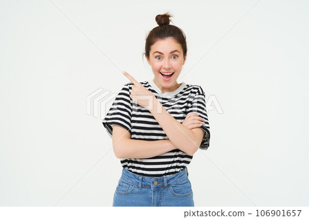 Image of excited young woman, smiling, showing amazing price discounts, pointing left, demonstrating something awesome, standing over white background 106901657