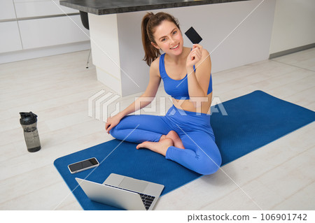 Portrait of young fitness girl paying for online class subscription, workout app, holding credit card, sitting on yoga mat with laptop, buying fitness tutorials Portrait of young fitness girl paying for online class subscription, workout app, holding credit card, sitting on yoga mat with laptop, buying fitness tutorials 106901742