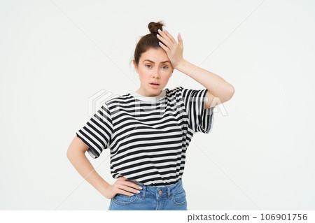 Shocked woman, slaps her forehead, holds hand on head and looks startled, concerned re something bad, terrible situation, standing over white background Shocked woman, slaps her forehead, holds hand on head and looks startled, concerned re something bad, terrible situation, standing over white background 106901756