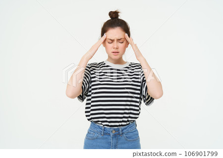 Health and wellbeing. Young woman suffering headache, touching her head, feeling discomfort, takes painkillers, stands over white background Health and wellbeing. Young woman suffering headache, touching her head, feeling discomfort, takes painkillers, stands over white background 106901799