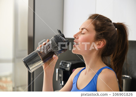 Close up portrait of sportswoman face, fitness girl drinks water from sport bottle and smiling, hydrating after productive aerobics, yoga workout 106901826