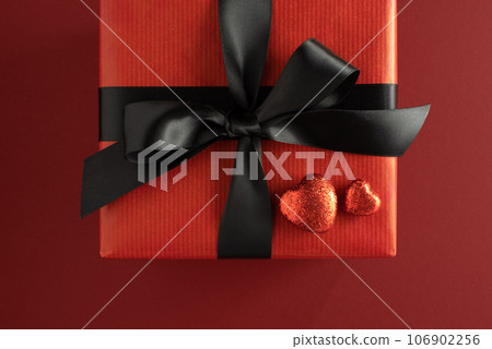 Part of gift box with red bow and two red shiny hearts on red background. Present for Valentine's Day. 106902256