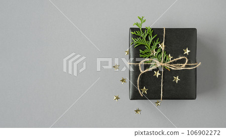 Black gift box with thuja and confetti on a gray background. Flatly, copyspace. Black gift box with thuja and confetti on a gray background. Flatly, copyspace. 106902272