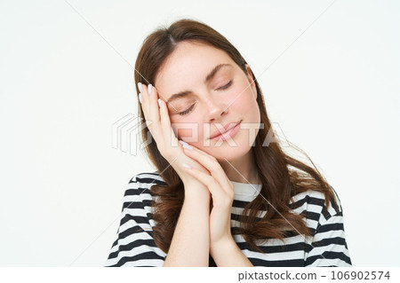 Close up portrait of tender, smiling young woman, closes her eyes and touches her palm, sleeping on her hand, isolated on white background Close up portrait of tender, smiling young woman, closes her eyes and touches her palm, sleeping on her hand, isolated on white background 106902574