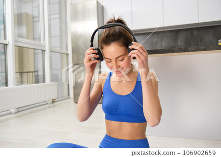 Young woman doing workout training at home, puts on her wireless headphones Young woman doing workout training at home, puts on her wireless headphones 106902659