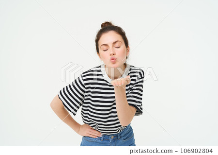 Portrait of beautiful brunette woman sends air kiss at camera, holds palm near lips, isolated against white background Portrait of beautiful brunette woman sends air kiss at camera, holds palm near lips, isolated against white background 106902804