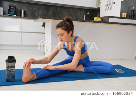 Image of young fit woman, does gymanstics at home, stretches her legs on floor in living room, does fitness workout, yoga warm-up exercises Image of young fit woman, does gymanstics at home, stretches her legs on floor in living room, does fitness workout, yoga warm-up exercises 106902884