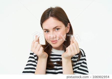 Portrait of cute young brunette woman, shows kawaii finger hearts and smiling, likes smth, stands in striped t-shirt over white background Portrait of cute young brunette woman, shows kawaii finger hearts and smiling, likes smth, stands in striped t-shirt over white background 106902954