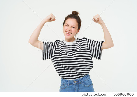 Woman power and feminism. Young girl feeling empowered and strong, flexing her biceps, showing muscles on arms, standing over white background Woman power and feminism. Young girl feeling empowered and strong, flexing her biceps, showing muscles on arms, standing over white background 106903000