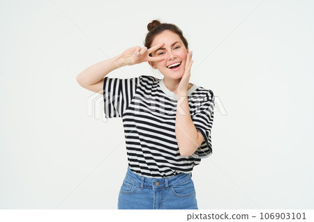 Cute european woman posing for photo, holding peace, kawaii hand gesture near face, smiling at camera, standing over white background 106903101