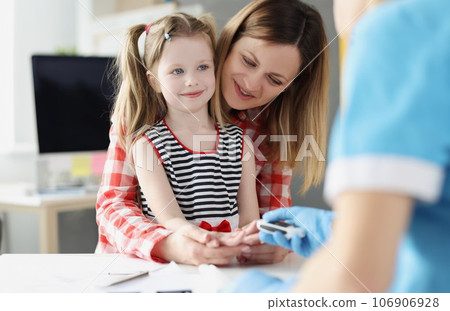 Doctor checks blood sugar level of little girl using digital glucometer at hospital 106906928