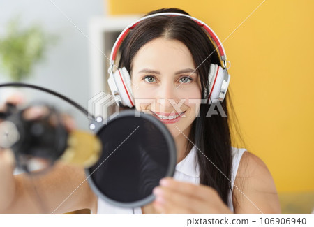 Portrait of smiling woman in headphones in front of microphone in studio Portrait of smiling woman in headphones in front of microphone in studio 106906940