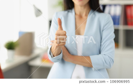 Businesswoman in suit holds thumbs up in office Businesswoman in suit holds thumbs up in office 106906995