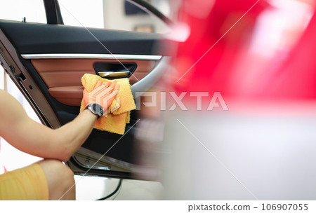 Male hand hold yellow microfiber towel and wipes the door with leather panel closeup 106907055