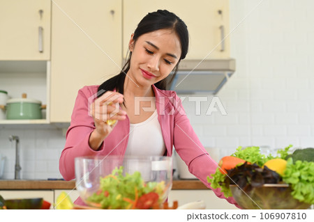 Charming sporty woman making a healthy salad in kitchen. Healthy food, dieting and loosing weight concept 106907810