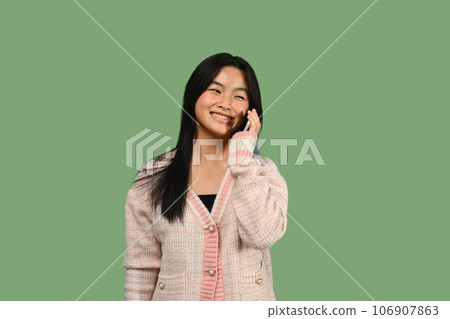 Pleasant teenage talking on mobile phone against green background. People, technology and communication Pleasant teenage talking on mobile phone against green background. People, technology and communication 106907863