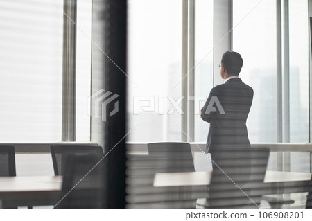 rear side view of an asian business man standing in front of office window looking out and thinking rear side view of an asian business man standing in front of office window looking out and thinking 106908201