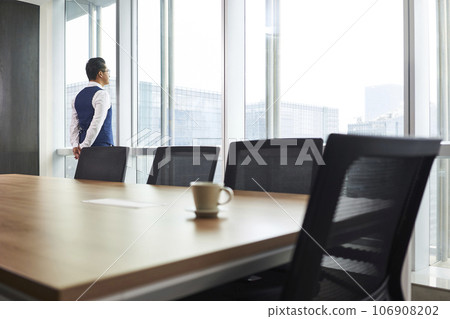 asian corporate executive standing in front of window thinking in company conference room asian corporate executive standing in front of window thinking in company conference room 106908202