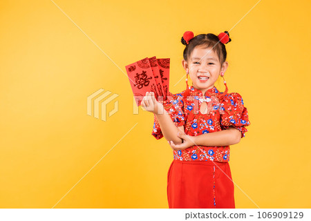 Chinese New Year. Happy Asian Chinese little girl smile wear red cheongsam qipao hold angpao red packet monetary gift, Portrait child in traditional dress, studio short isolated on yellow background Chinese New Year. Happy Asian Chinese little girl smile wear red cheongsam qipao hold angpao red packet monetary gift, Portrait child in traditional dress, studio short isolated on yellow background 106909129